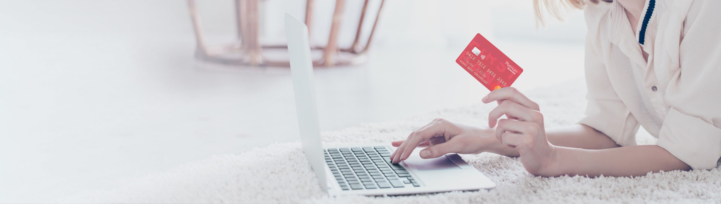 a woman holding her Ariston Credit Union Platinum Rewards card while on the computer.