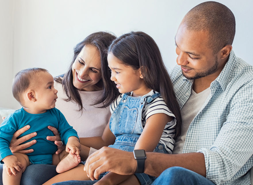 A family of four, smiling at one another.