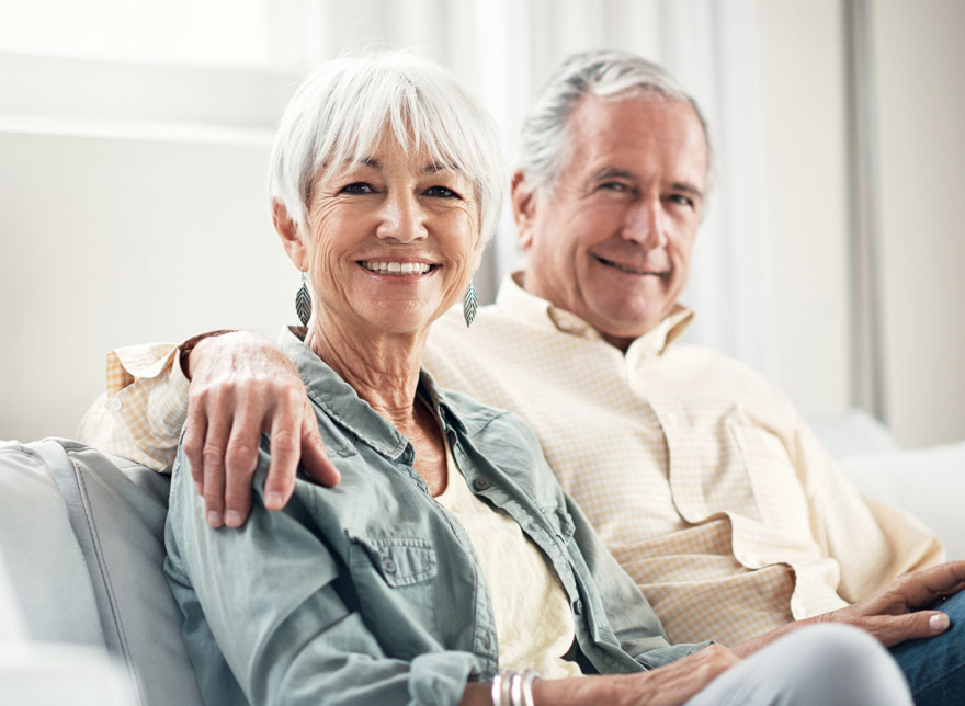 Senior aged man and woman smiling in living room.